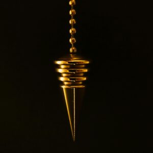 An elegant gold pendulum with chain on a mysterious black background.