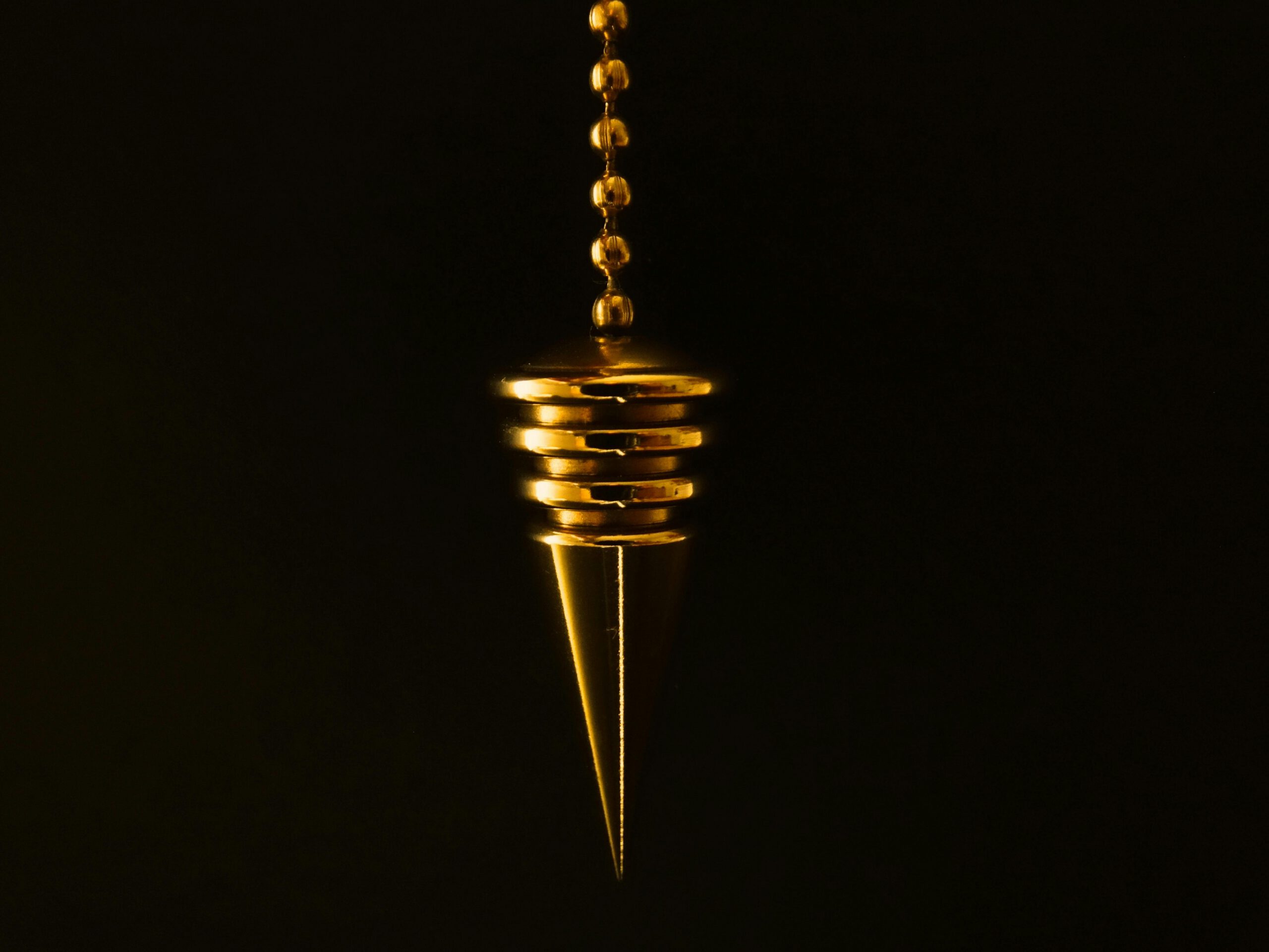 pendulum cone chain gold 39239 39239 An elegant gold pendulum with chain on a mysterious black background.