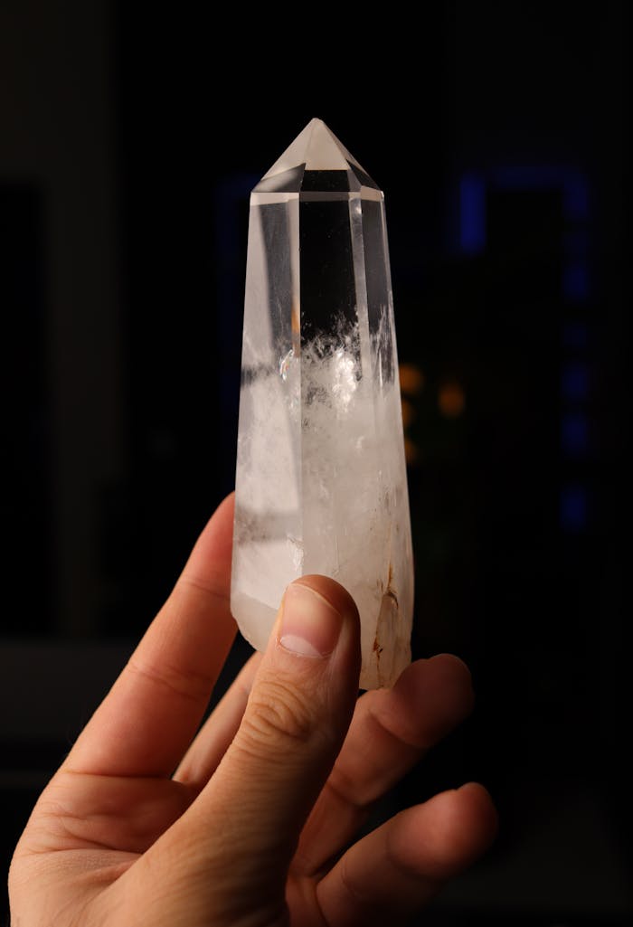 services-02 Close-up of a hand holding a clear quartz crystal tower against a dark background.